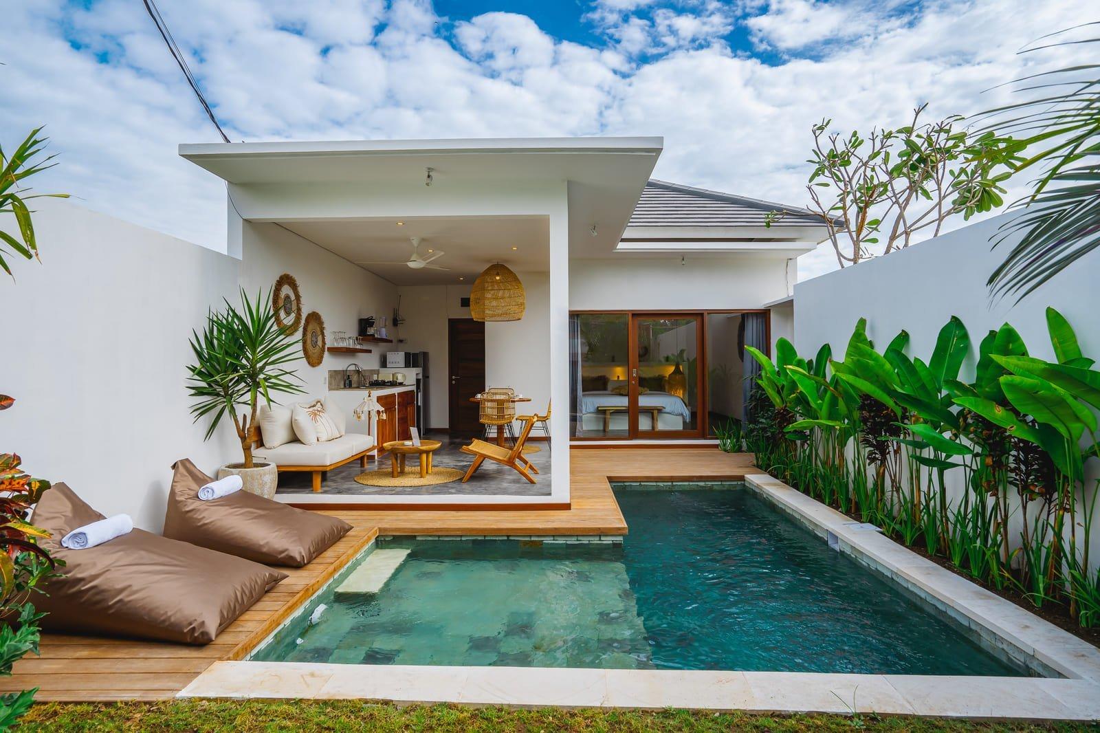 Intérieur d'une villa deux chambres à Bali avec piscine privée, mobilier en bois naturel et grandes baies vitrées ouvrant sur un jardin tropical luxuriant