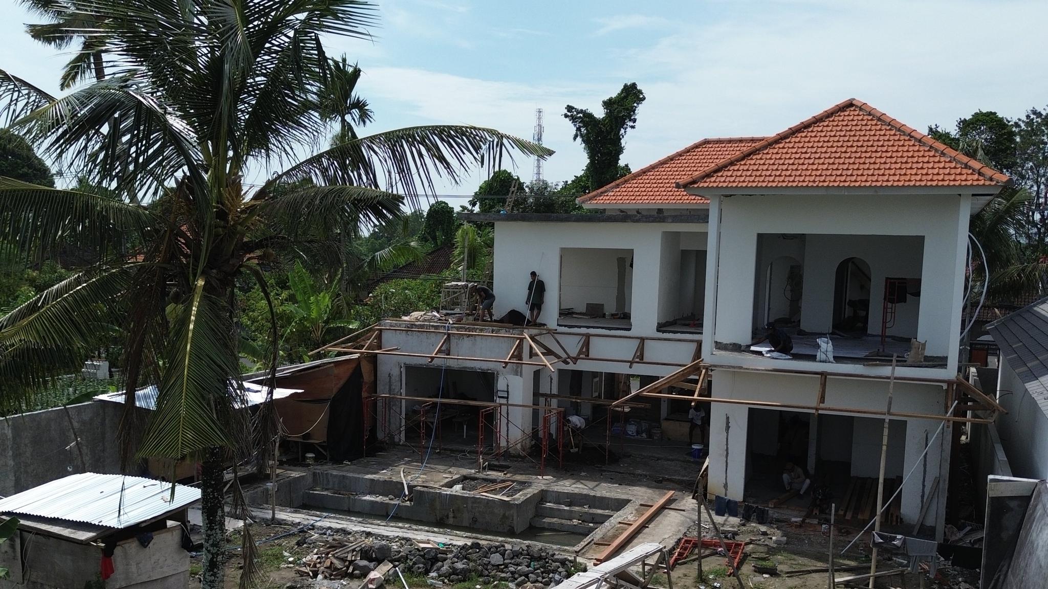 Vue d'une villa moderne à deux niveaux avec piscine rectangulaire, mobilier extérieur en teck et jardin tropical à Canggu, Bali, en plein après-midi sous un ciel clair