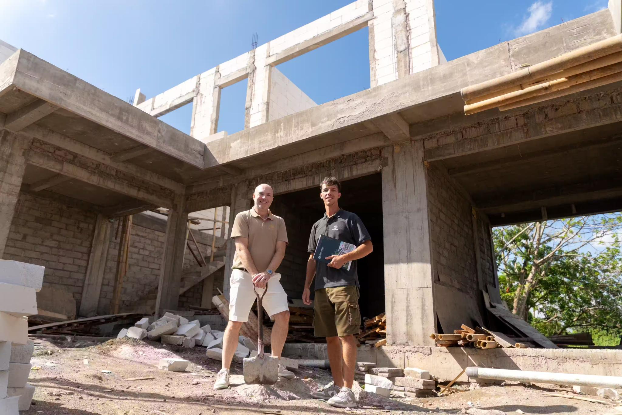 Chantier de construction d'une villa balinaise contemporaine avec ossature en béton et charpente bois, ouvriers sur l'échafaudage, entouré de végétation tropicale dense sous un ciel couvert